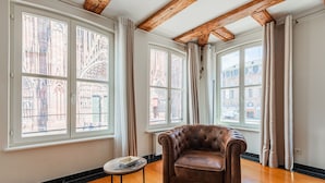 A room with a leather armchair, wooden flooring, and large windows with curtains. - La Place de la Cathédrale - Superbe appt face à la Cathédrale (Strasbourg)