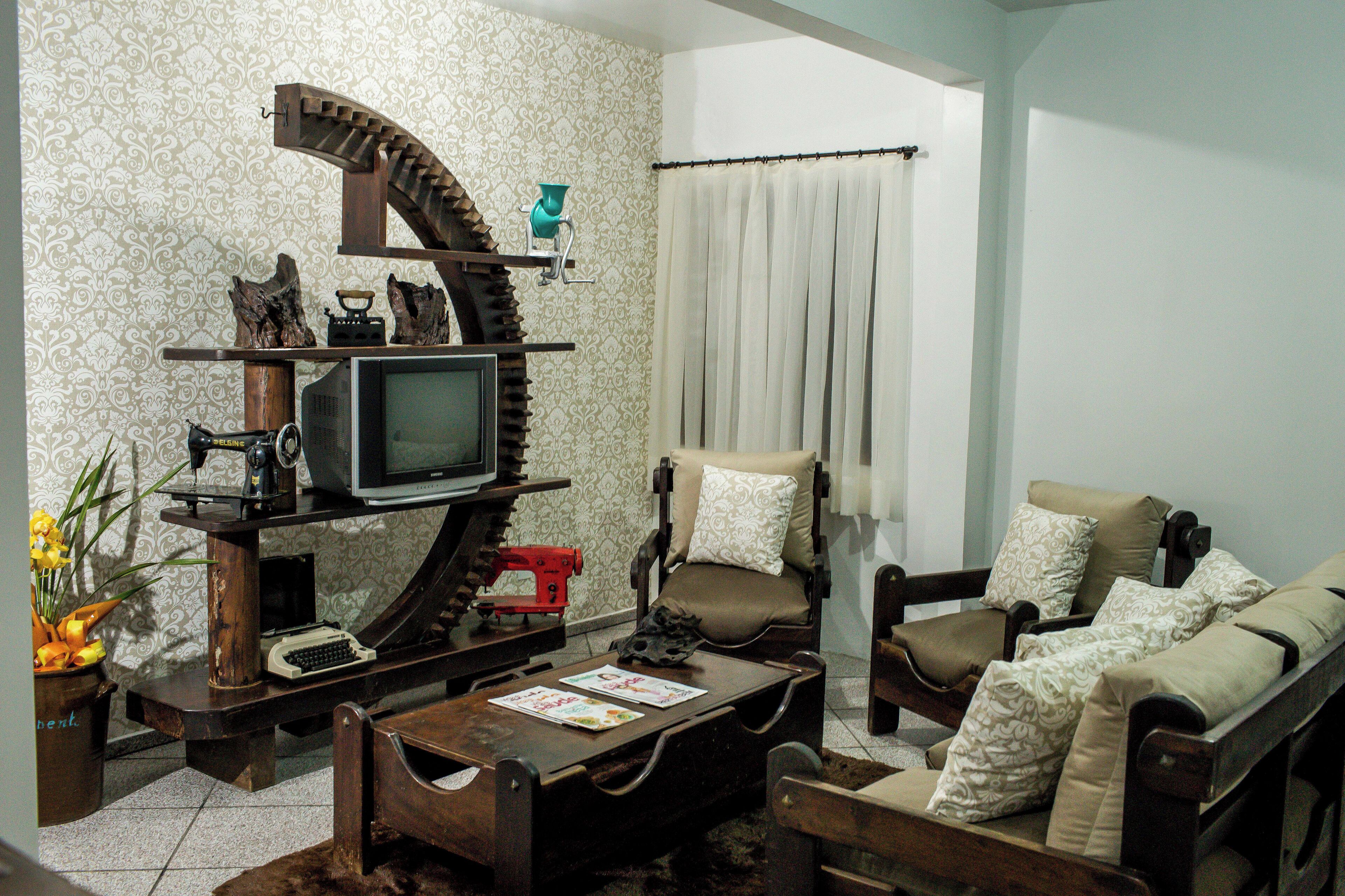 Uma sala de estar com televisão, móveis de madeira, uma poltrona, um sofá e papel de parede estampado.