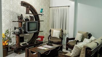 Uma sala de estar com televisão, móveis de madeira, uma poltrona, um sofá e papel de parede estampado.