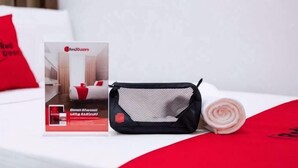 Una cama con una almohada roja, una bolsa de malla negra y una toalla enrollada.