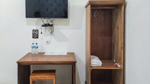 Una habitación pequeña con un escritorio de madera, un televisor montado en la pared, un armario de madera y un pequeño banco.