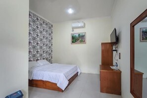 Un dormitorio con cama, una mesita de noche de madera, aire acondicionado, televisor y una pared con diseño geométrico.