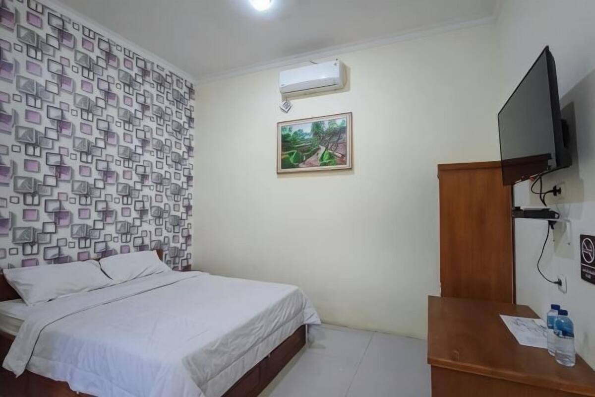 Un dormitorio con una cama, un televisor, un escritorio de madera y un aire acondicionado instalado en la pared.