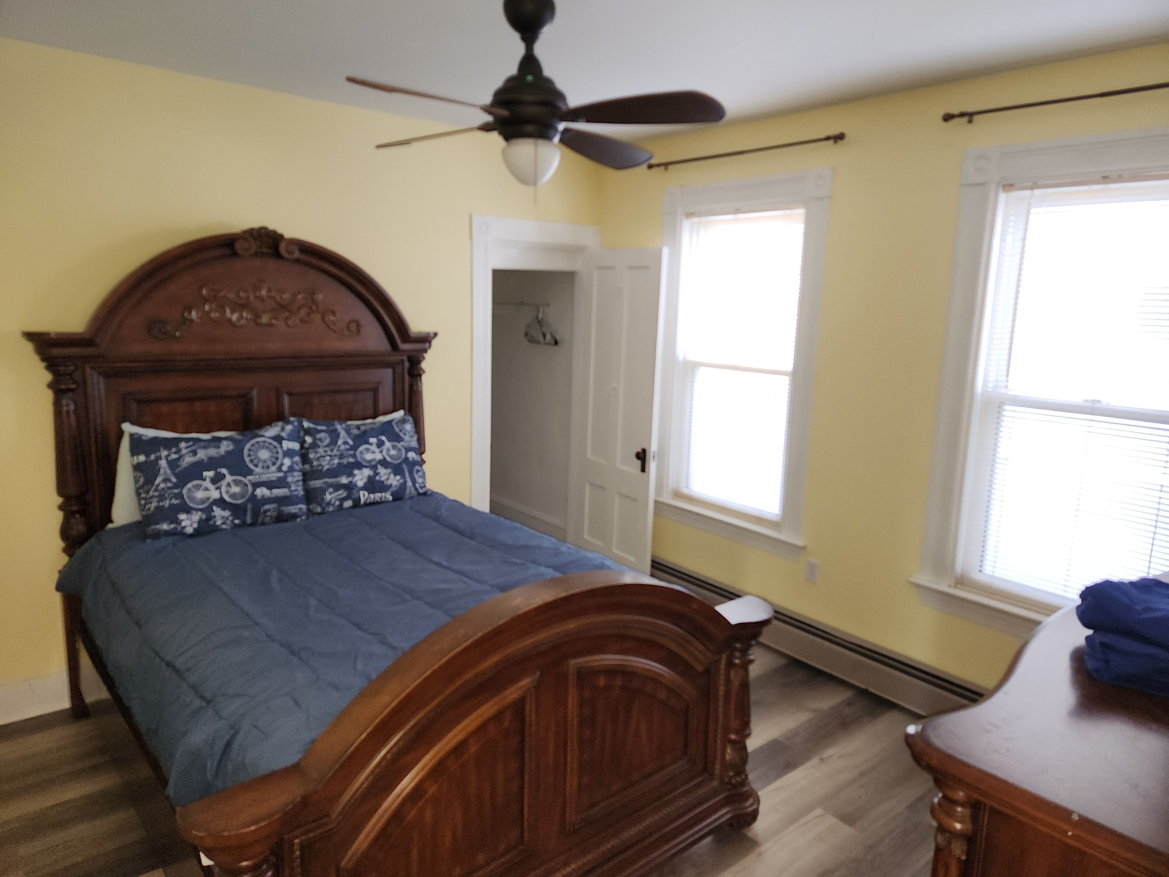 Un dormitorio con una cama de madera, un ventilador de techo y dos ventanas con persianas.