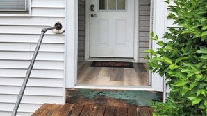 A white front door with a glass panel, a wooden porch with steps, and a green plant to the right. - Very spacious, clean, and comfortable first floor unit. Close to major highway!  (Manchester)