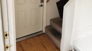 A hallway with a white door, a staircase with a dark handrail, and a framed picture on the wall. - Very spacious, clean, and comfortable first floor unit. Close to major highway!  (Manchester)