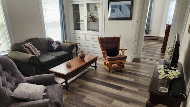 A living room with a sofa, armchair, wooden coffee table, and a chair with a cushion. - Very spacious, clean, and comfortable first floor unit. Close to major highway!  (Manchester)