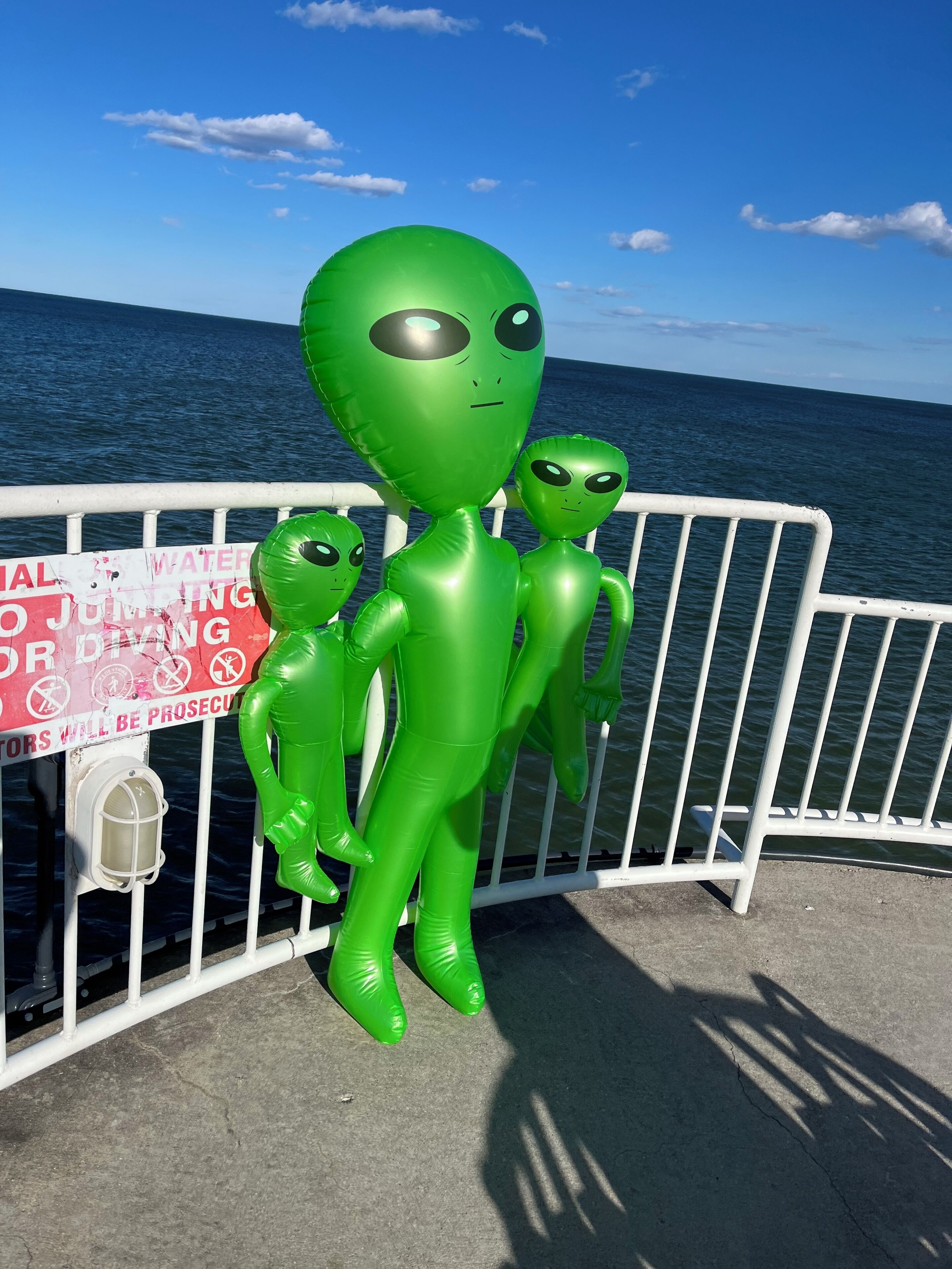 Inflatable alien figures near a railing with a warning sign about water jumping.