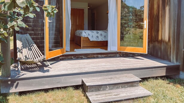 Een houten hut met een houten terras, een bed met hemelbed en uitzicht op de natuur.