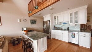 Een moderne keuken met witte kasten, een marmeren eiland en een houten plafond.