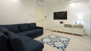 Uma sala de estar com um sofá seccional azul escuro, um móvel de entretenimento branco com uma TV de tela plana e um tapete estampado.