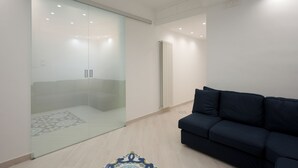Uma sala de estar moderna com divisória de vidro, um sofá escuro e um tapete estampado.