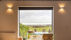 A room with a glass table and chairs, a view of the beach, and two wall-mounted lights.