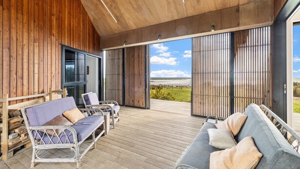A wooden deck with outdoor seating, large sliding glass doors, and a view of the landscape.