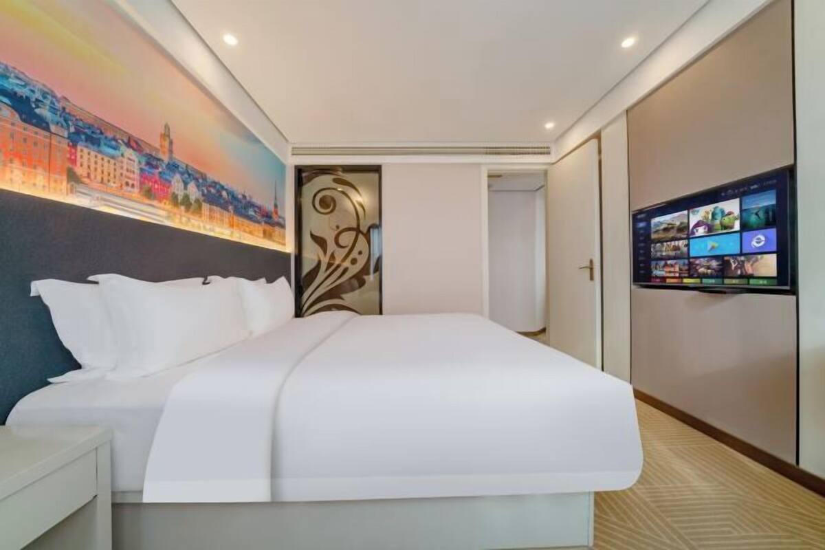 A hotel room with a large bed, a television on the wall, and a decorative wall panel.