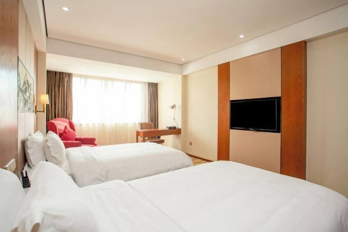 A hotel room with two beds, a TV mounted on the wall, a desk, and a chair.