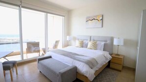 A bedroom with a large bed, two bedside tables, a chair, and a view of the sea. - Jolla Excellence 3bd 2b Rosarito (Playas de Rosarito)