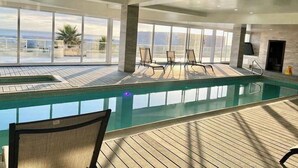 A spacious indoor swimming pool with clear views of the ocean, surrounded by large windows and modern seating. - Jolla Excellence 3bd 2b Rosarito (Playas de Rosarito)