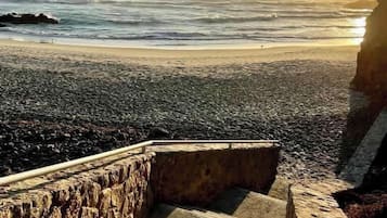 A dog on a stone staircase overlooking a beach with waves and a sunset.