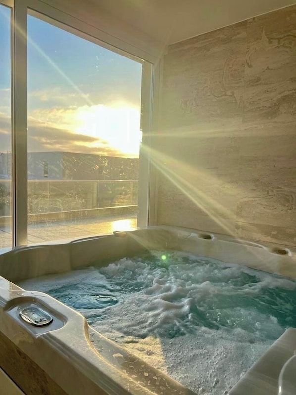 A hot tub with a view of the sunset through a window.