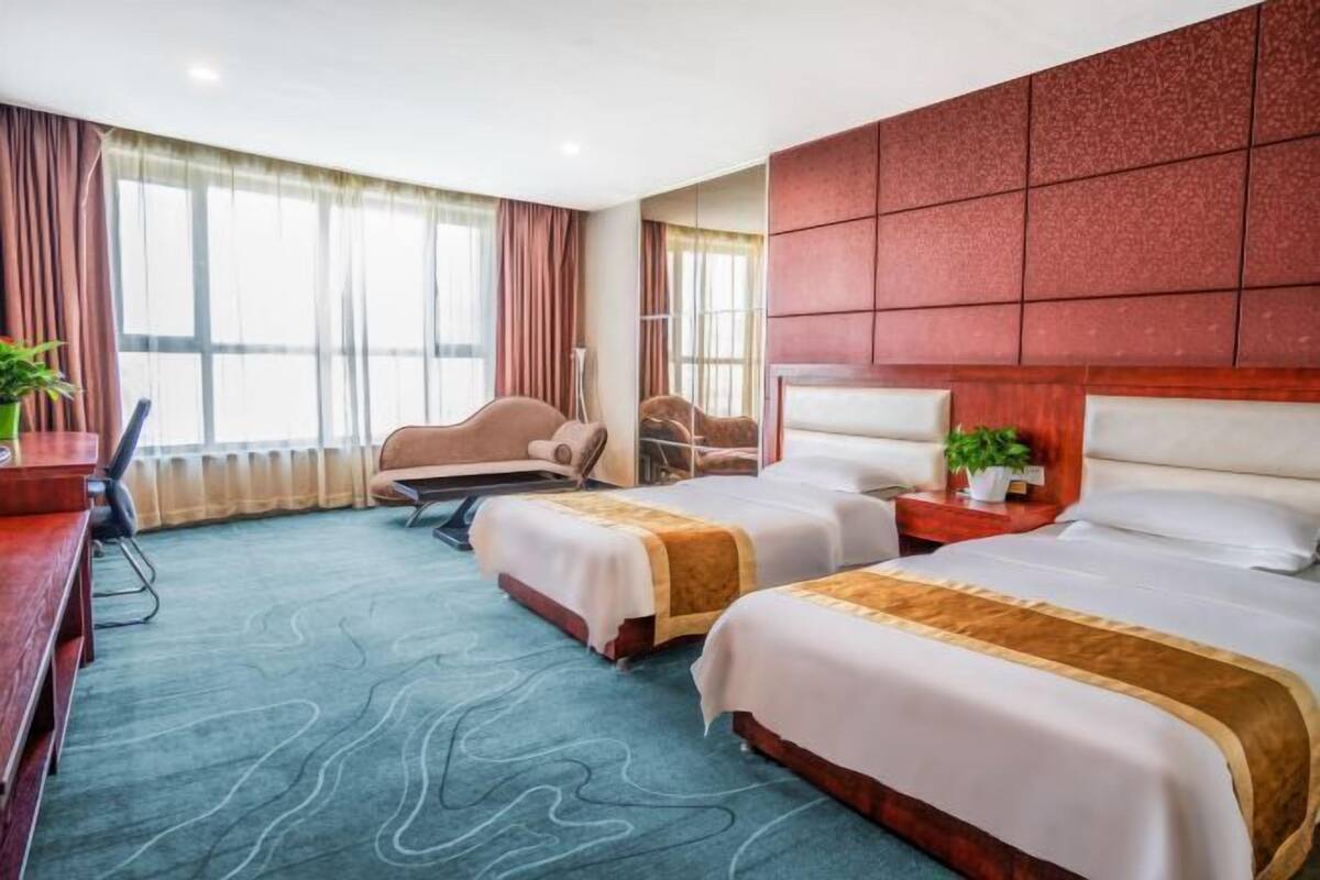 Habitación de hotel con dos camas, un escritorio, una silla y un ventanal con cortinas.
