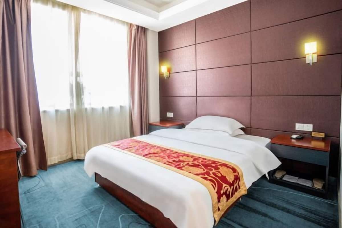 Habitación de hotel con una cama grande, una mesita de noche, un escritorio y una ventana con cortinas.