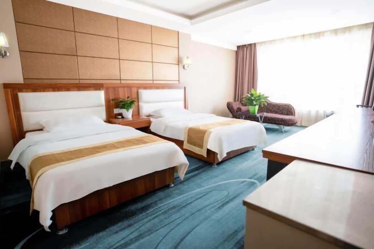 Habitación de hotel con dos camas, un escritorio, una silla y un ventanal grande.