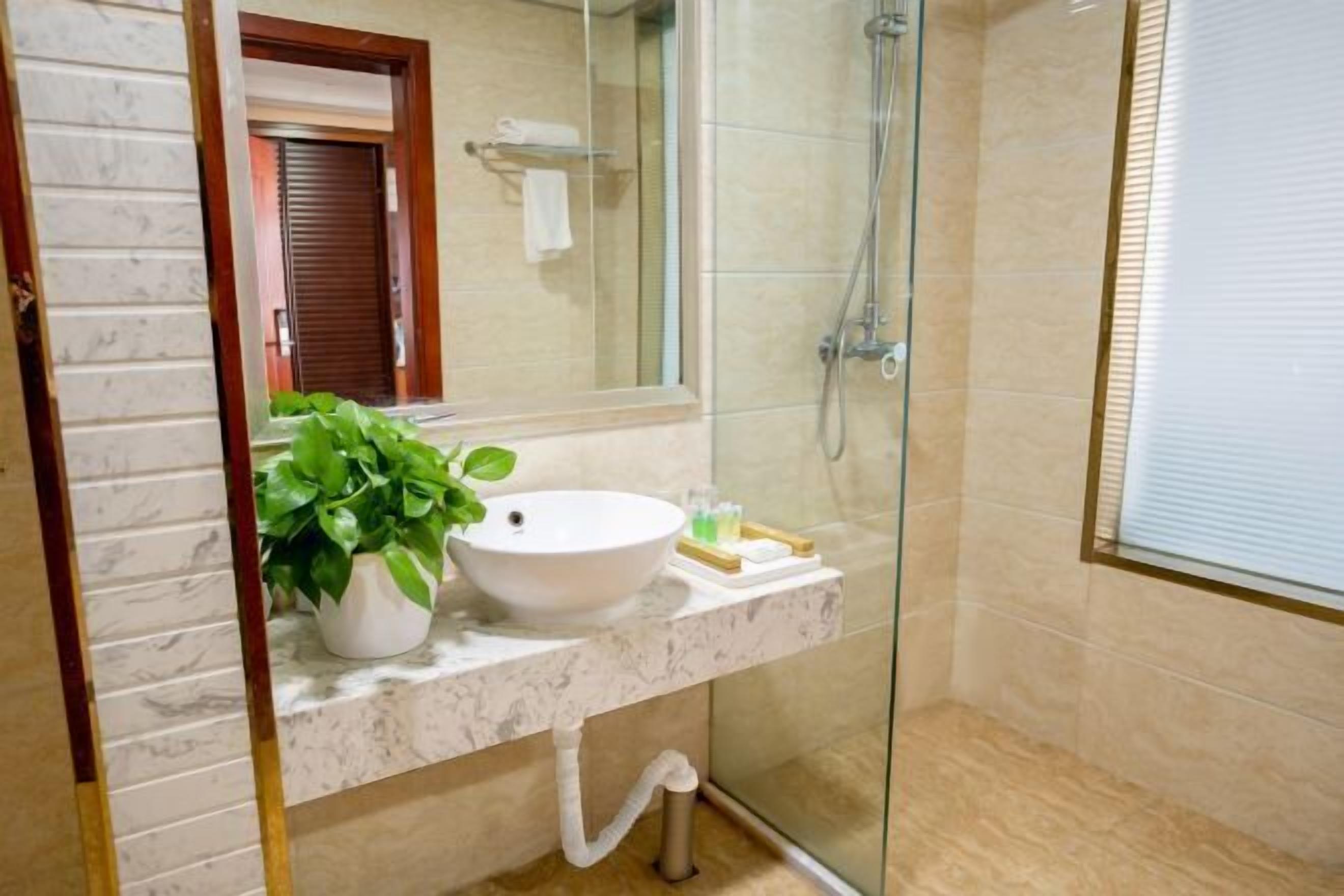 Een badkamer met een witte wastafel, een potplant, een glazen douchecabine en een marmeren aanrechtblad.