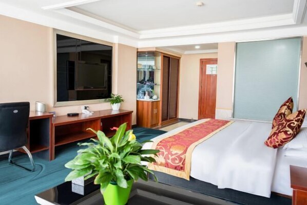 A hotel room with a bed, a desk, a chair, a mirror, a wardrobe, and a potted plant. - Shangcheng Business Hotel (Korla)
