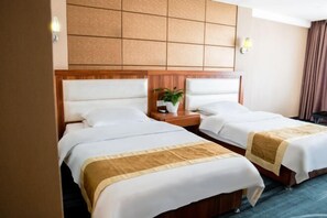 Two double beds with wooden headboards, a small bedside table with a plant, and a wall-mounted light fixture. - Shangcheng Business Hotel (Korla)