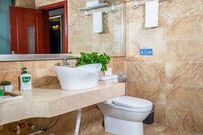 A bathroom with a marble wall, a white sink, a toilet, a mirror, and a towel rack. - Shangcheng Business Hotel (Korla)