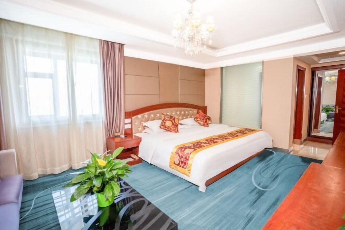 A hotel room with a large bed, a nightstand, a glass coffee table, and a potted plant.