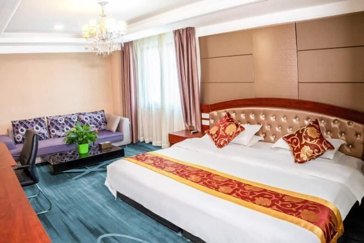 Una habitación de hotel con una cama grande, un sofá, un escritorio y una araña.