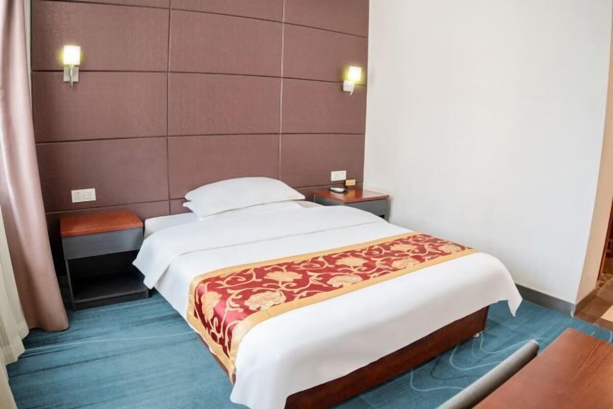 A hotel room with a bed, a nightstand, a lamp, and a wooden bench.