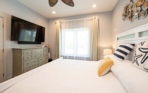 Una camera da letto con un letto grande, una TV a schermo piatto montata a parete, un comò e una finestra con tende.