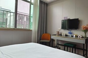 Habitación de hotel con cama, escritorio con televisor de pantalla plana, una silla y una mesita con un jarrón de flores.