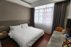 Una habitación de hotel con cama, escritorio, silla, teléfono y ventana con cortinas.