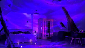 Une pièce avec un lit, une table et une chaise, dotée d’un plafond étoilé et d’un éclairage violet.