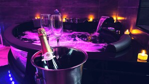 Un jacuzzi rempli d’eau chaude, avec du champagne et des verres, entouré de bougies et équipé d’une installation pour DJ.