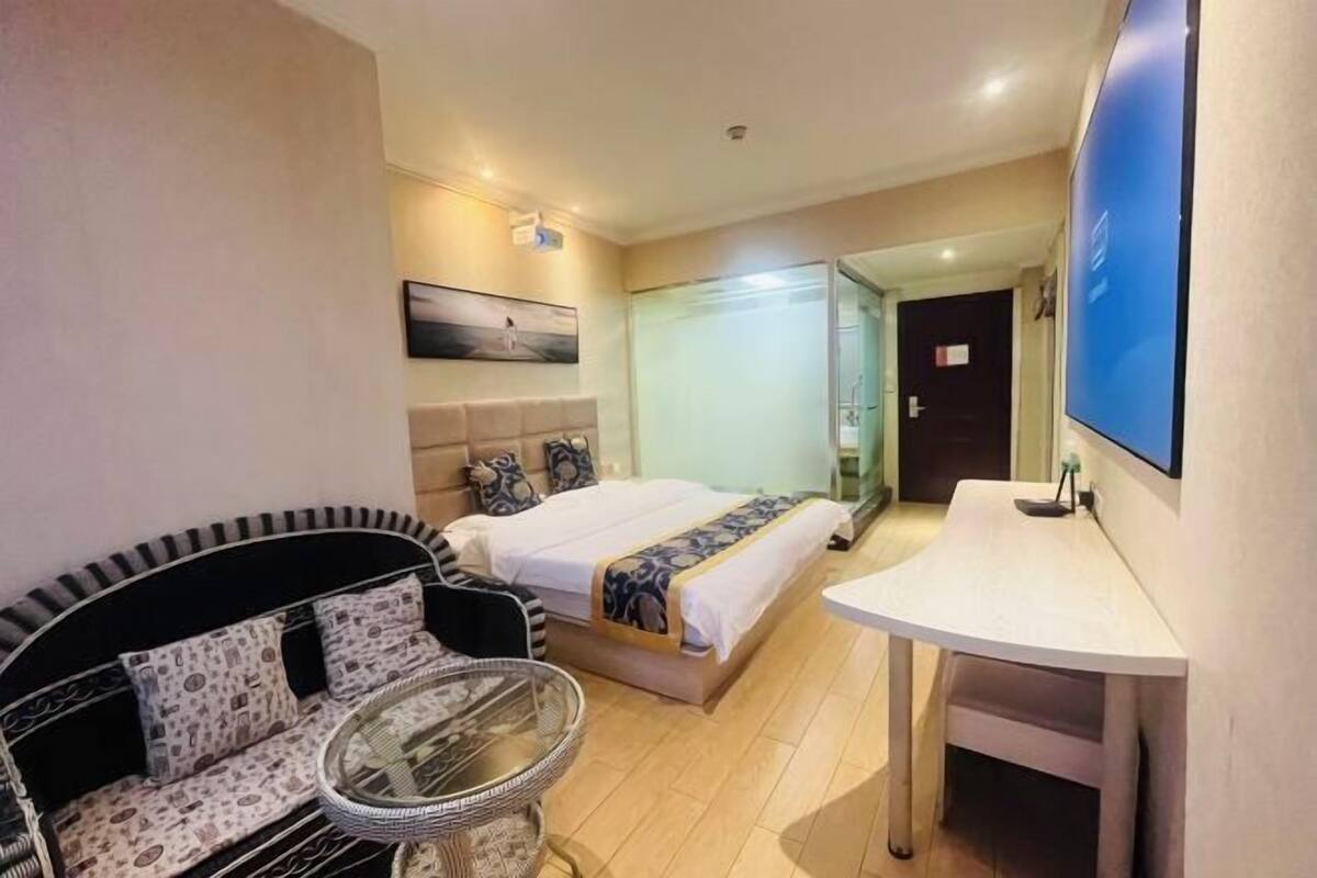 Quarto de hotel com cama, sofá, mesa pequena, televisão e porta do banheiro.