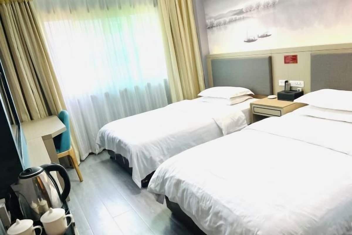Quarto de hotel com duas camas, uma escrivaninha, uma cadeira e uma chaleira.