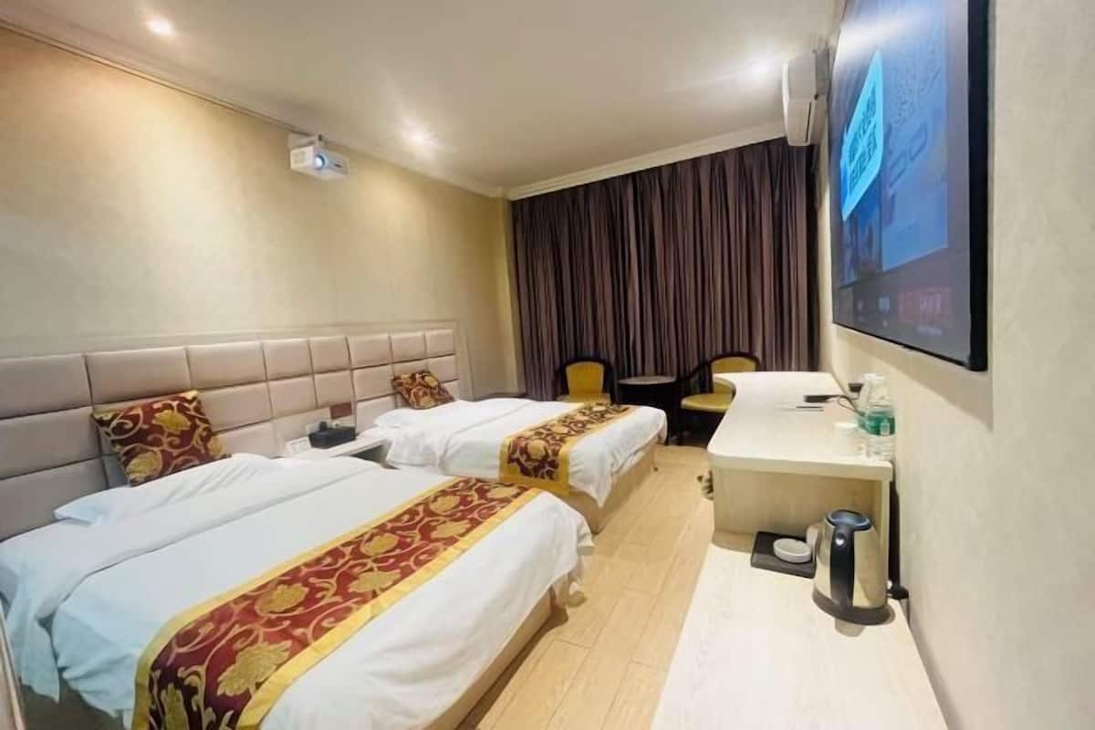 Quarto de hotel com duas camas, uma escrivaninha, uma cadeira, televisão e janela com cortinas.