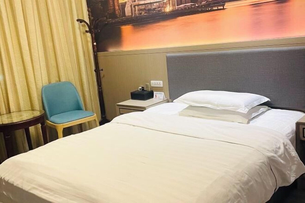 Habitación de hotel con cama, una silla, una mesita de noche y un mural en la pared.