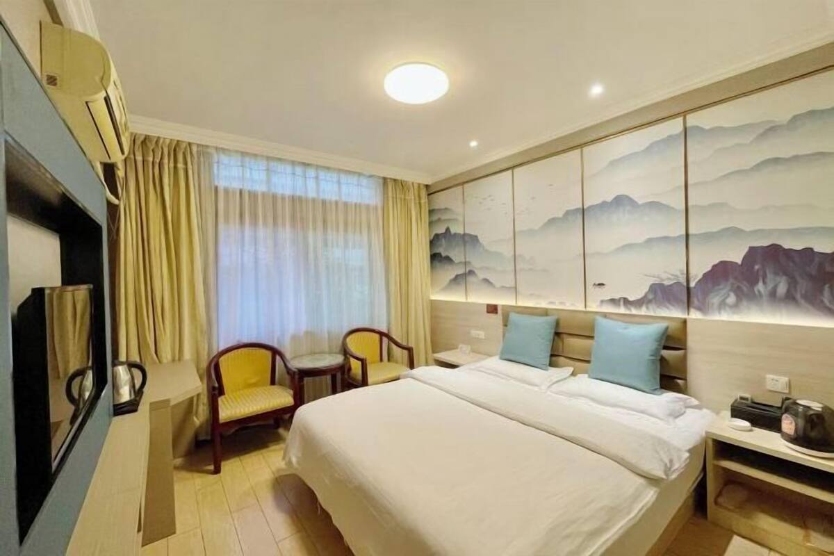 Quarto de hotel com uma cama grande, uma escrivaninha com cadeira, uma televisão e um quadro na parede.