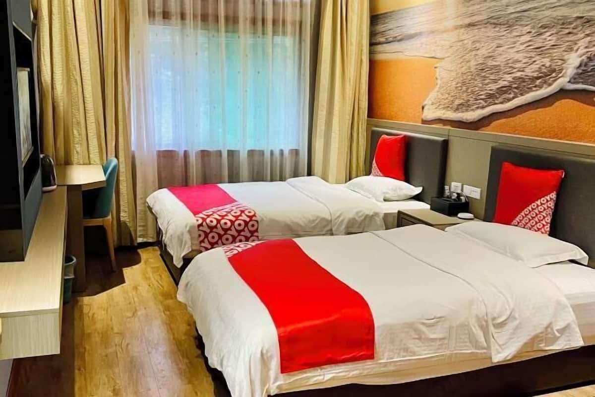 Quarto de hotel com duas camas, cada uma com roupa de cama branca e detalhes vermelhos, piso de madeira, uma escrivaninha e um mural grande na parede.