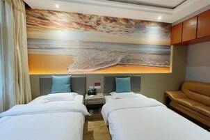 Habitación de hotel con dos camas, una mesita de noche, una lámpara y un mural grande con motivos playeros en la pared.