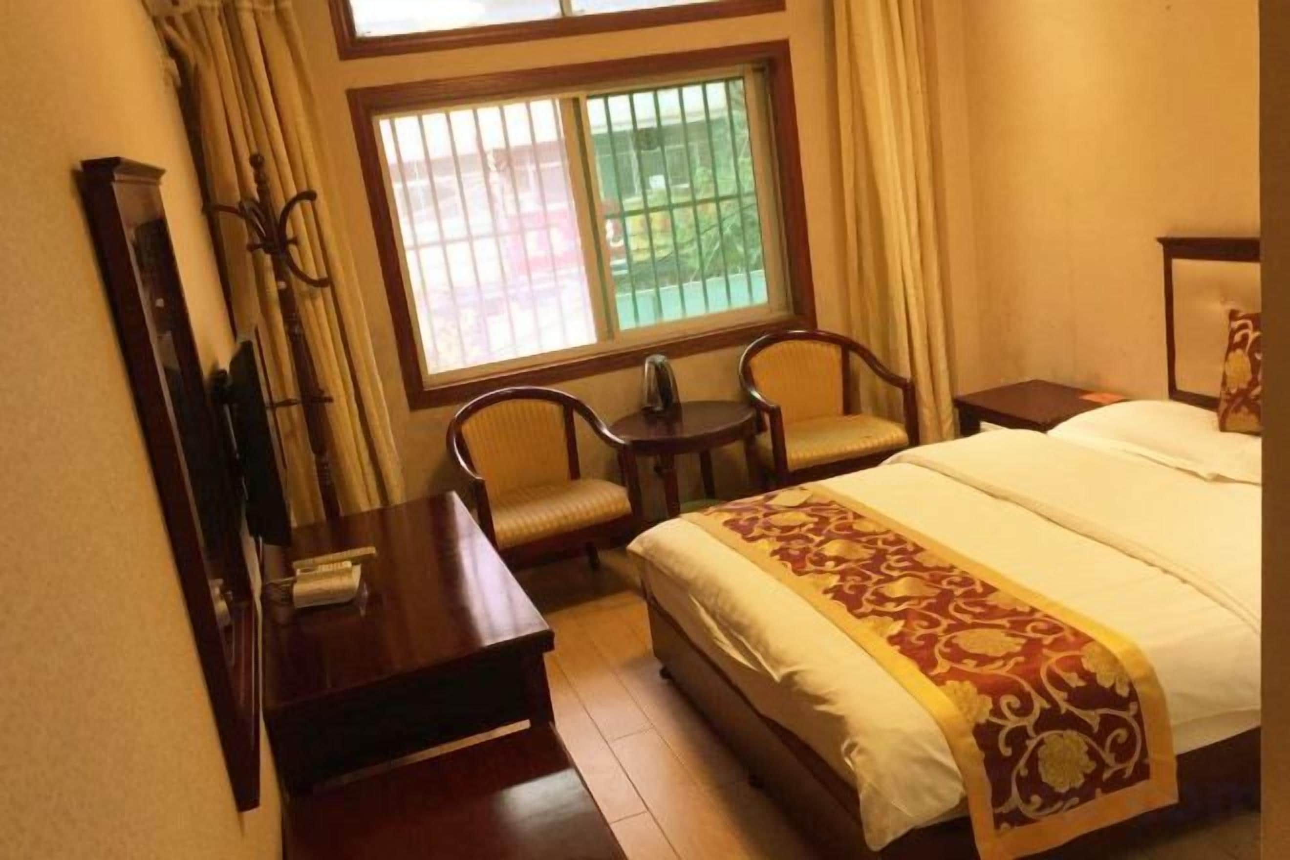 A hotel room with a bed, a desk, two chairs, a window with curtains, and a nightstand.