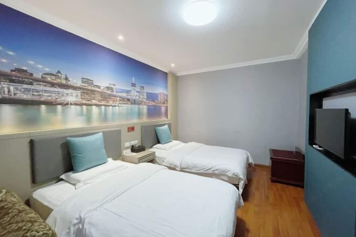 Quarto de hotel com duas camas, uma mesa de cabeceira, uma TV e um mural com vista para a cidade.