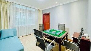 Una habitación de hotel con una cama, una mesa de comedor con sillas, un ventanal con cortinas y una puerta.