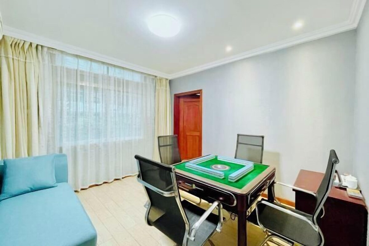Una habitación de hotel con una cama, una mesa de comedor con sillas, un ventanal con cortinas y una puerta.